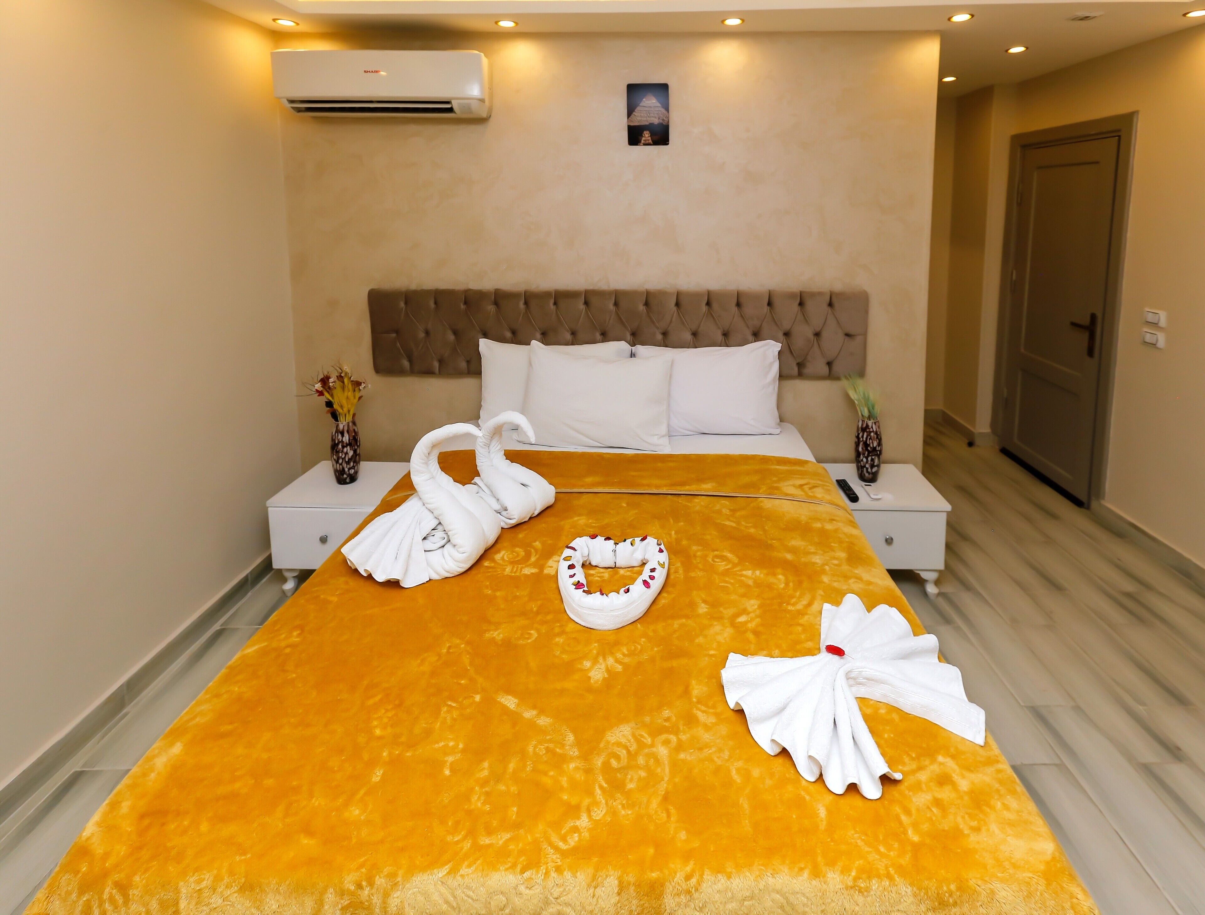 Una habitación de hotel con una cama grande, dos mesitas de noche, aire acondicionado, un cuadro colgado en la pared y una puerta.