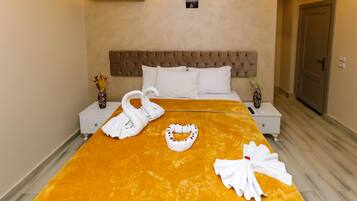 Una habitación de hotel con una cama grande, dos mesitas de noche, aire acondicionado, un cuadro colgado en la pared y una puerta.