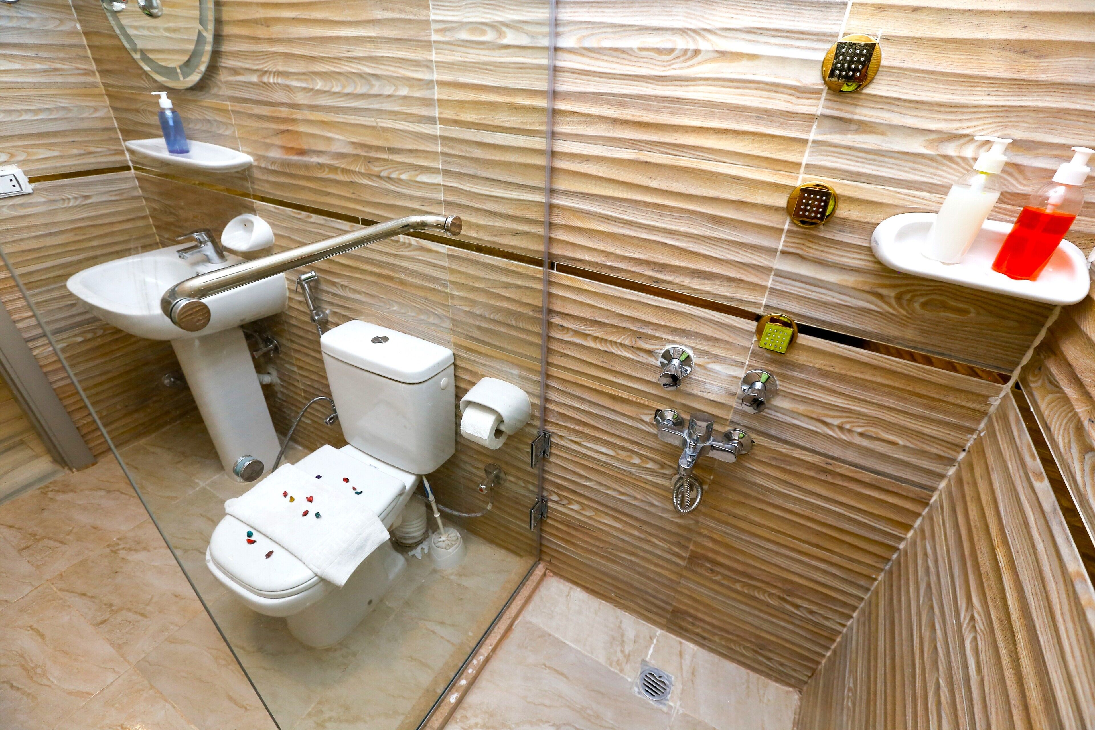 A modern bathroom with a wooden wall design, a glass shower enclosure, a white sink, and a toilet with a grab bar.