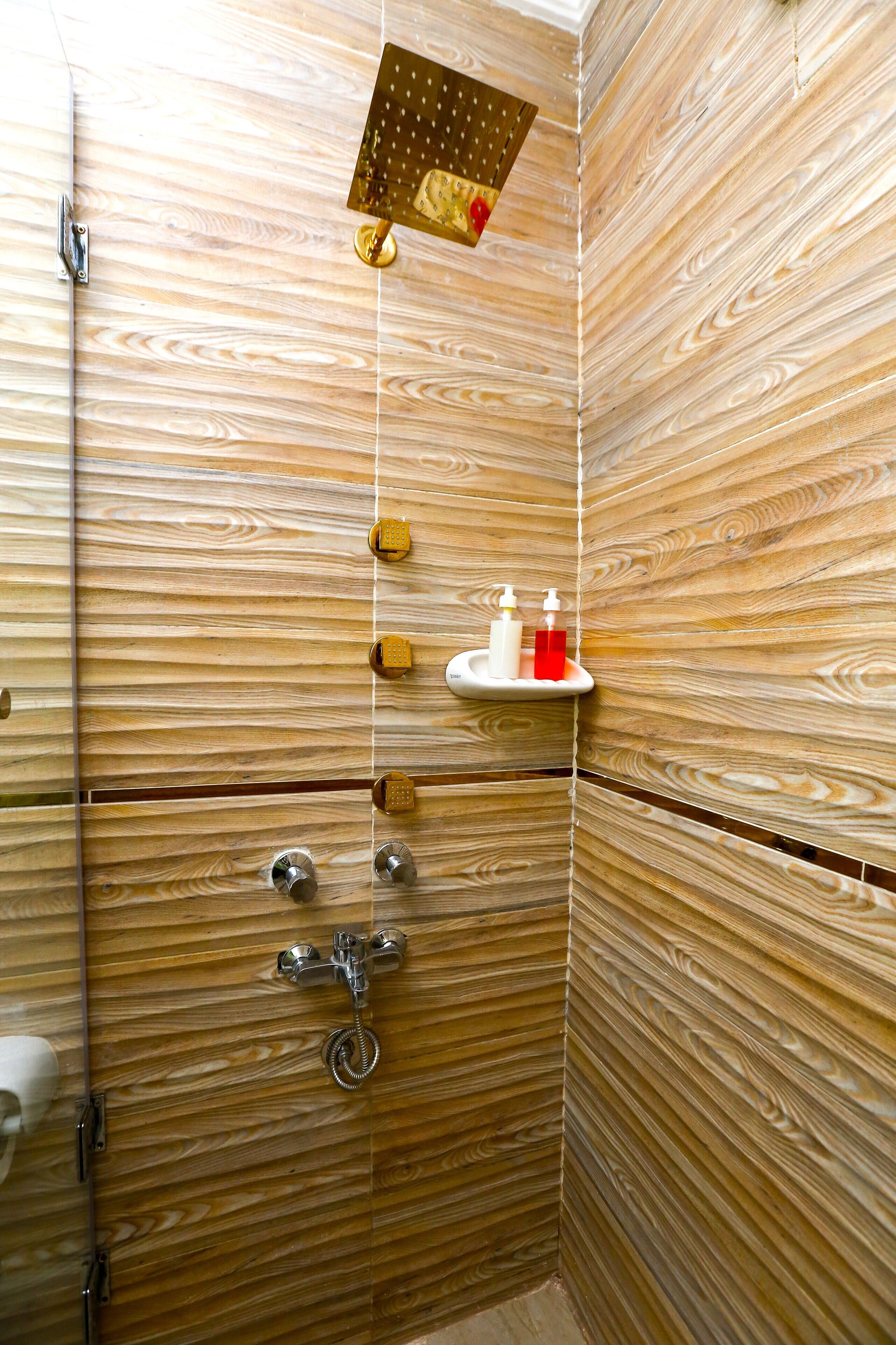 A wooden-paneled shower stall with a handheld showerhead, a towel rack, and a soap dispenser on a shelf.