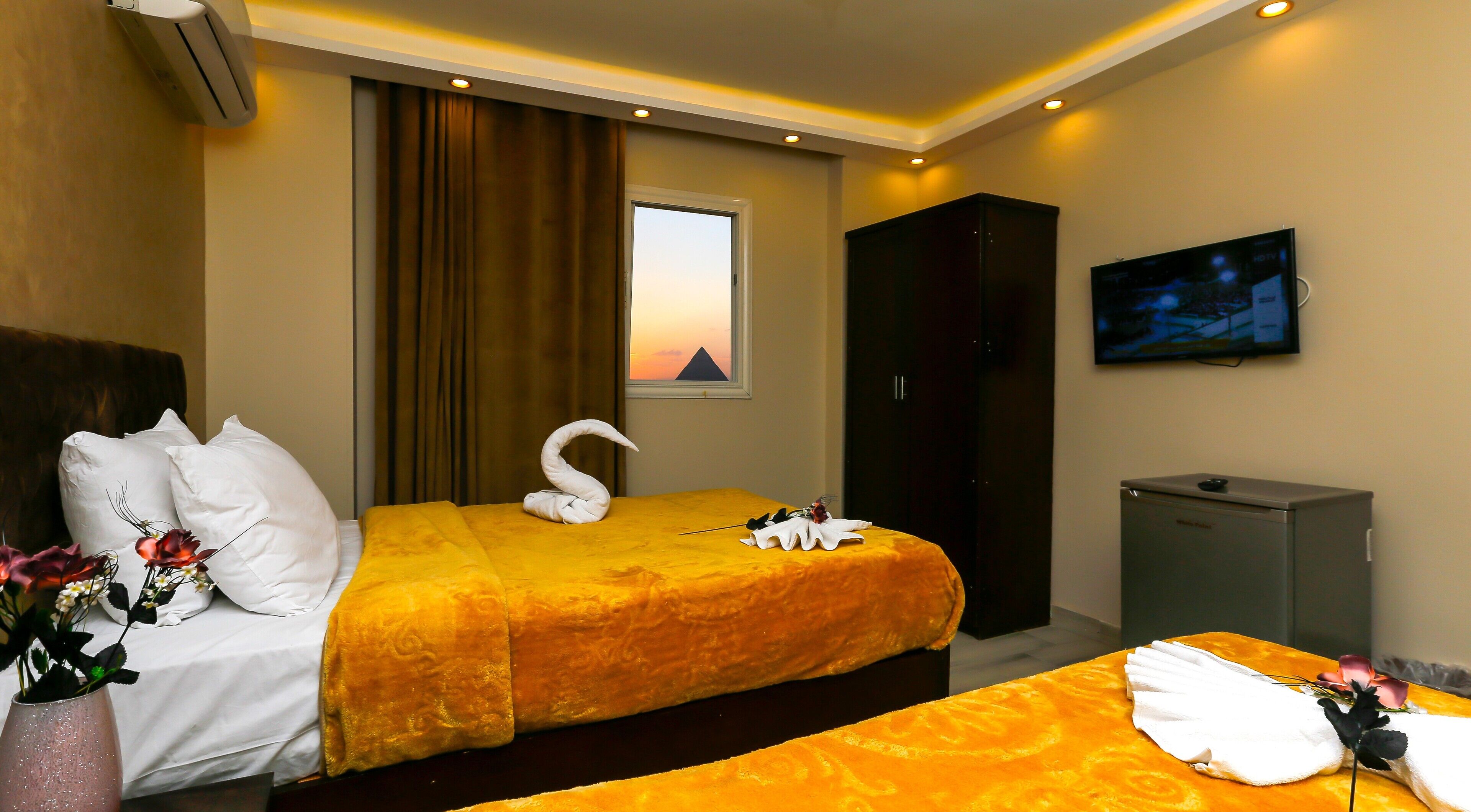 Ett hotellrum med två sängar, ett stort fönster med utsikt över en pyramid, en tv på väggen och en minibar.