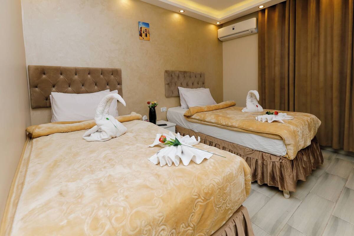 A hotel room with two beds, each with a plush headboard and a decorative towel.