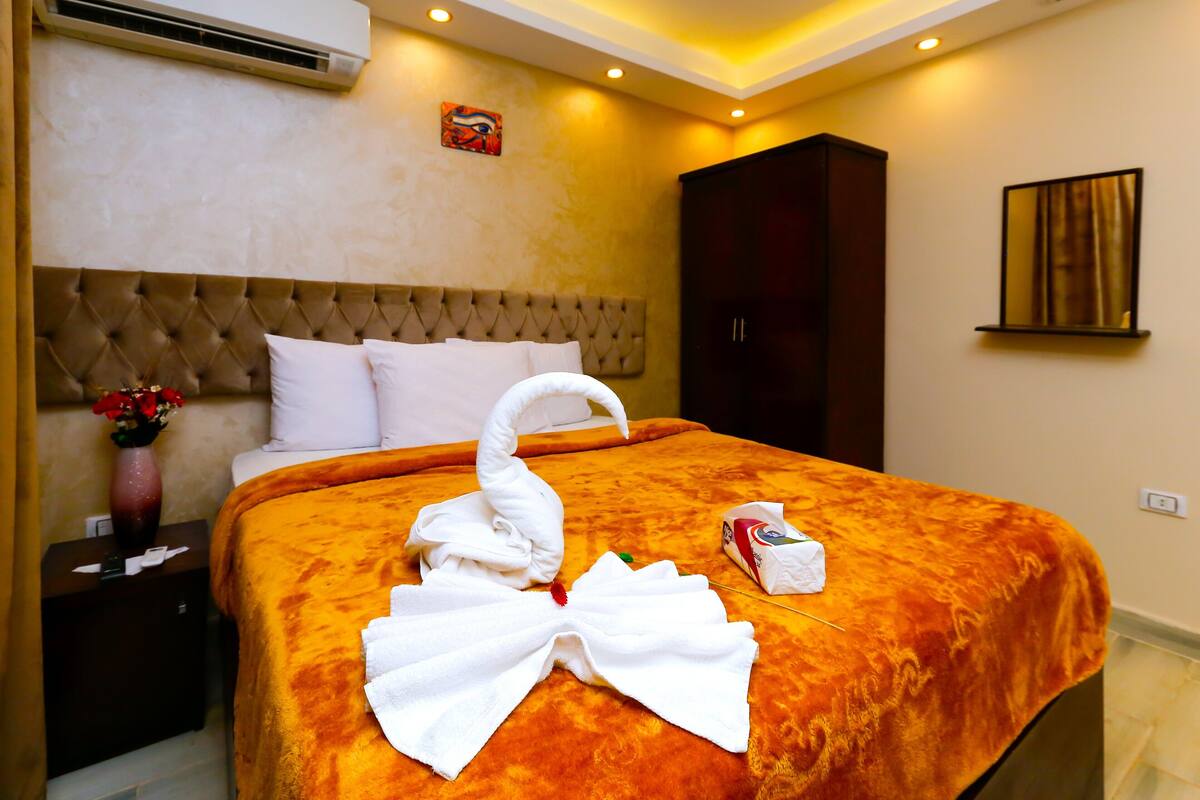 A hotel room with a large bed, a dark wooden wardrobe, and a wall-mounted air conditioner.
