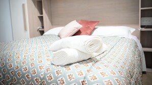 Un lit bien fait, recouvert d’une couvre-lit à motifs, avec une paire de serviettes enroulées et deux oreillers.