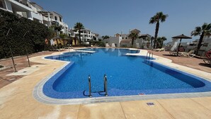 Piscina com borda azulejada, cercada por espreguiçadeiras e palmeiras.