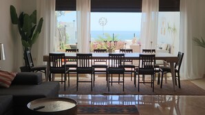 Uma sala de estar moderna com área de jantar, janelas amplas e vista para o mar.