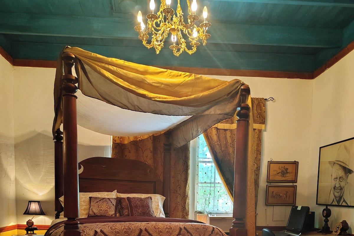 A four-poster canopy bed with a patterned bedspread, a wooden floor, and a chandelier.