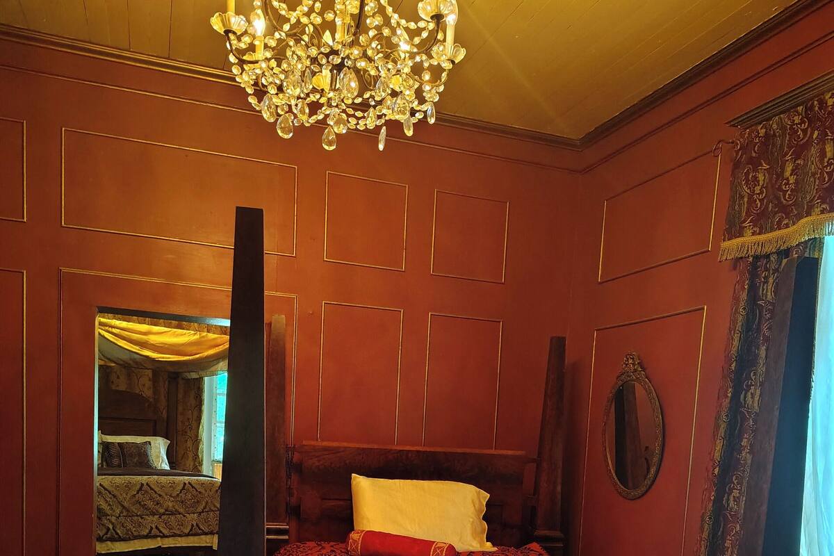 A room with a large bed, a chandelier, wooden paneling, and a mirror.