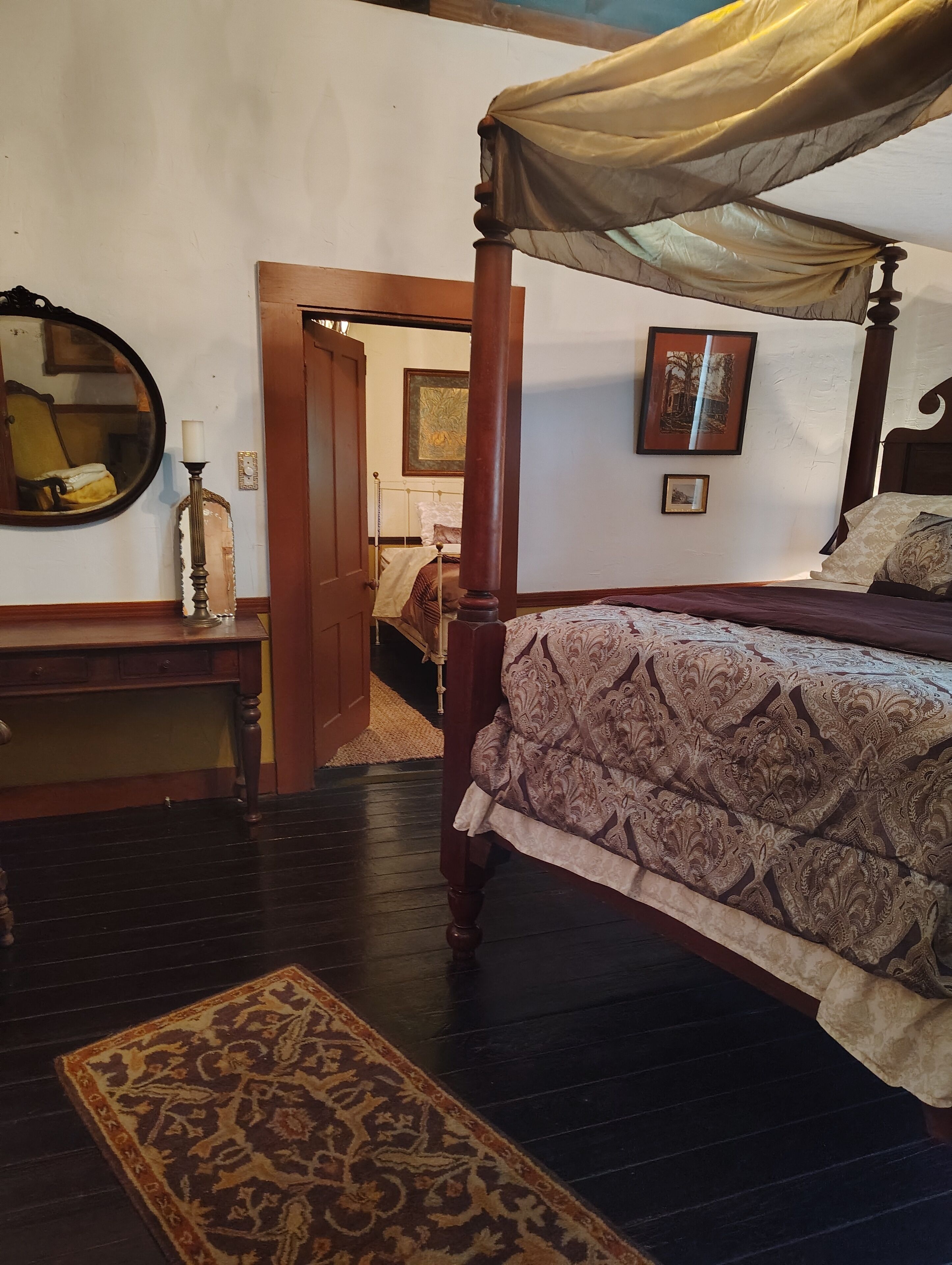 A traditional bedroom with a canopy bed, a round mirror, a bedside table, and a patterned rug.