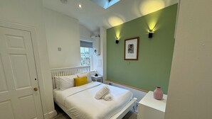 A bedroom with a white bed, a small bedside table, a green accent wall, and a skylight. - Angel Mews - Westend Glasgow Uni Cottage (Glasgow)