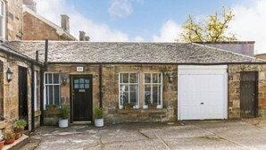 A stone building with a black door, two windows with shutters, and a white garage door. - Angel Mews - Westend Glasgow Uni Cottage (Glasgow)