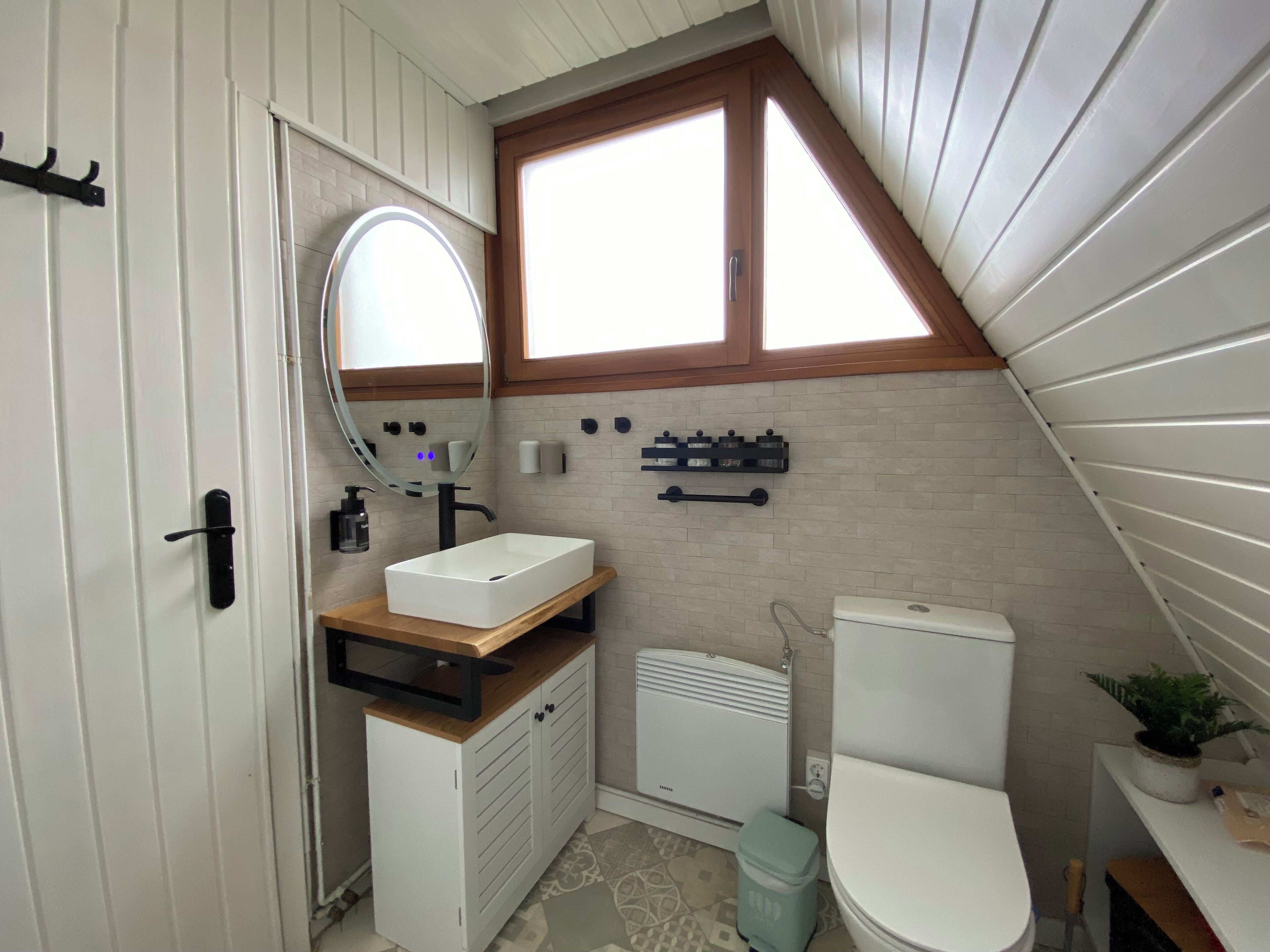Un baño pequeño con un lavamanos blanco, un espejo, un inodoro y una ventana.