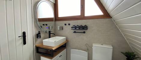 A compact bathroom with a white sink, a mirror, a toilet, and a window.
