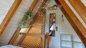 A bedroom with a sloped ceiling, wooden beams, a bed, a hanging plant, and a netted partition. - Renoviertes Nurdachhaus in Ostfriesischer Natur am Wasser für Familien (Südbrookmerland)