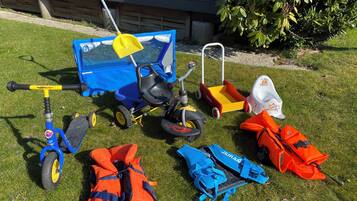Een gazon met diverse kinderspeelgoed en veiligheidsuitrusting, waaronder een driewieler, een autospeeltje en reddingsvesten.