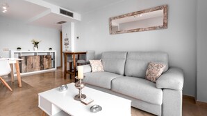Un salon moderne avec un canapé gris, une table basse blanche et un miroir décoratif accroché au mur.