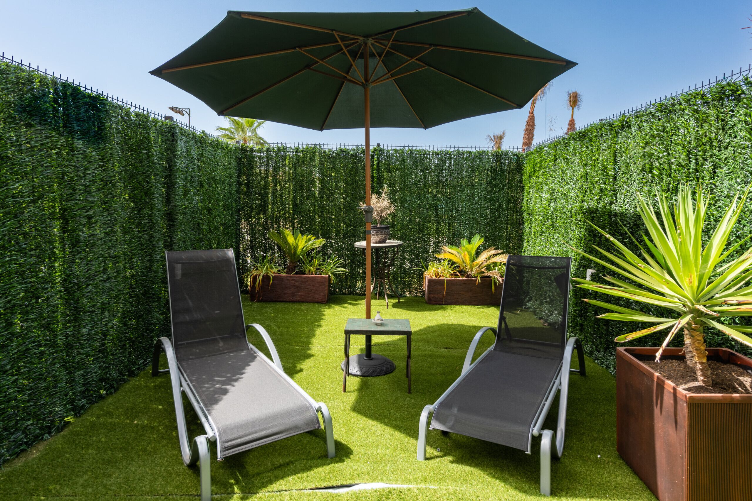 Een besloten tuin met twee loungesteunen, een tafel en een parasol.