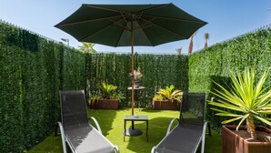 Un jardin privé avec deux chaises longues, une table et un parasol.