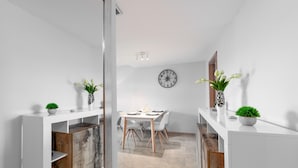 Un espace repas moderne avec une table blanche, des chaises et une horloge au mur.