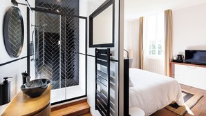 A modern hotel room with a shower, a sink, a bed, a TV, and a window with curtains.