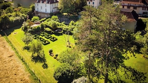 A well-maintained garden with geometric hedge patterns, surrounded by residential buildings and a body of water.