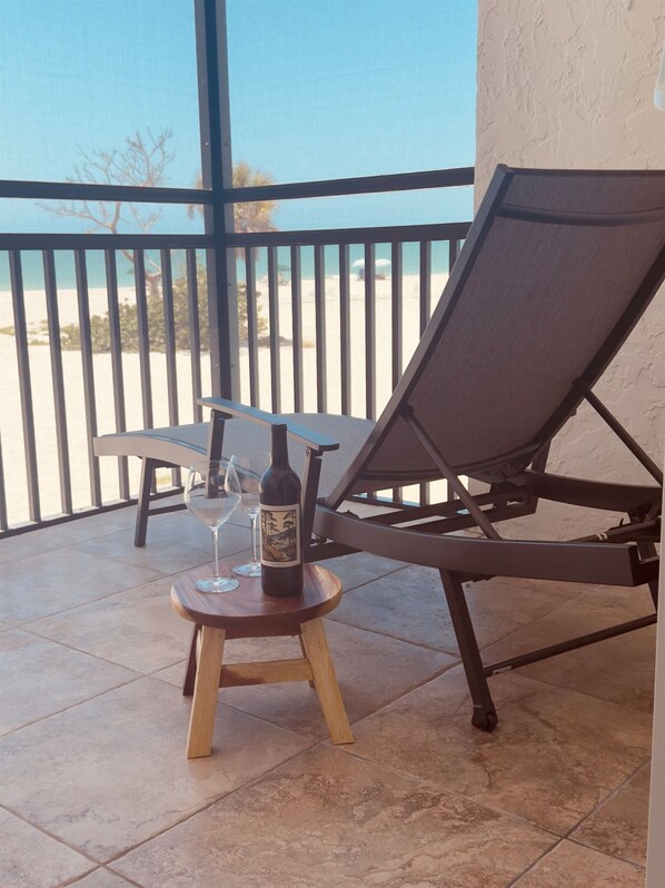 A balcony with a chair and a small table, a bottle of wine, and two wine glasses. - Sayana Unit 101 – Steps to Sand & Sunset Views (Sanibel)
