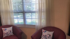 Two red armchairs with matching cushions, positioned in front of a window with blinds, allowing natural light to enter.