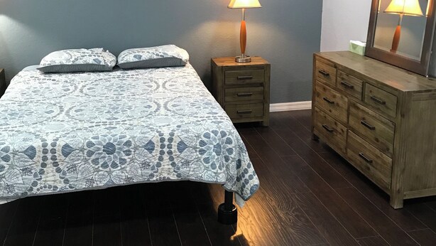 A bedroom with a bed, a nightstand, a dresser, a ceiling fan, and a wall-mounted lamp.