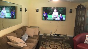 A living room with a brown couch, a glass coffee table, a red armchair, and a television mounted on the wall.