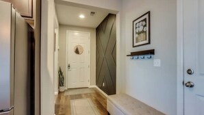 Un couloir avec un banc, une porte et un cadre photo fixé au mur.