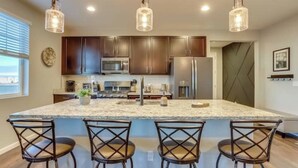 Une cuisine moderne avec des meubles en bois foncé, un îlot en granit doté de tabourets, des appareils électroménagers en acier inoxydable et des luminaires suspendus.