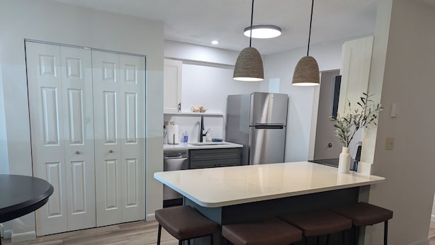 A modern kitchen with a central island, bar stools, a refrigerator, and pendant lighting. - Charming 2-bedroom condo in McHenry Close To Lake Activities and Ski Resort (McHenry)