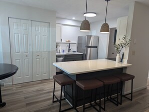 Una cucina moderna con isola centrale, sgabelli da bar, frigorifero e luci a sospensione.