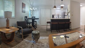 A modern living room with a glass coffee table, a dining area with a round table and chairs, and a kitchen with a bar. - Charming 2-bedroom condo in McHenry Close To Lake Activities and Ski Resort (McHenry)