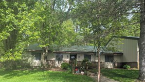 A two-story house with a green roof, surrounded by lush greenery and trees. - Charming 2-bedroom condo in McHenry Close To Lake Activities and Ski Resort (McHenry)