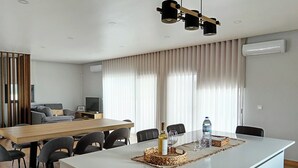 A modern living room with a dining area, featuring a wooden dining table, grey sofas, and a large window with curtains. - Casa de Lazer da Chã (Alqueidão da Serra)