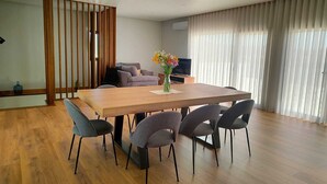 A modern dining area with a wooden table and grey chairs, a sofa, and a TV in the background. - Casa de Lazer da Chã (Alqueidão da Serra)