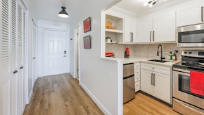 A modern kitchen with white cabinets, a stainless steel oven, and a microwave. - Stunning Studio Bay Views & Parking (North Bay Village)