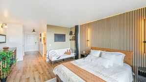 A modern bedroom with a large bed, a wooden headboard, a white sofa, and a wooden floor. - Stunning Studio Bay Views & Parking (North Bay Village)