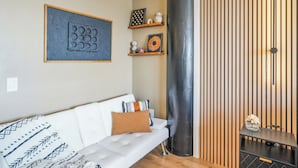 A modern living room with a white sofa, decorative pillows, a black cylindrical object, and wooden shelves with decorative items. - Stunning Studio Bay Views & Parking (North Bay Village)