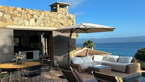 A patio with a stone wall, outdoor furniture, and a view of the ocean.