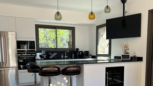 A modern kitchen with a central island, bar stools, a large window, and a flat-screen TV.