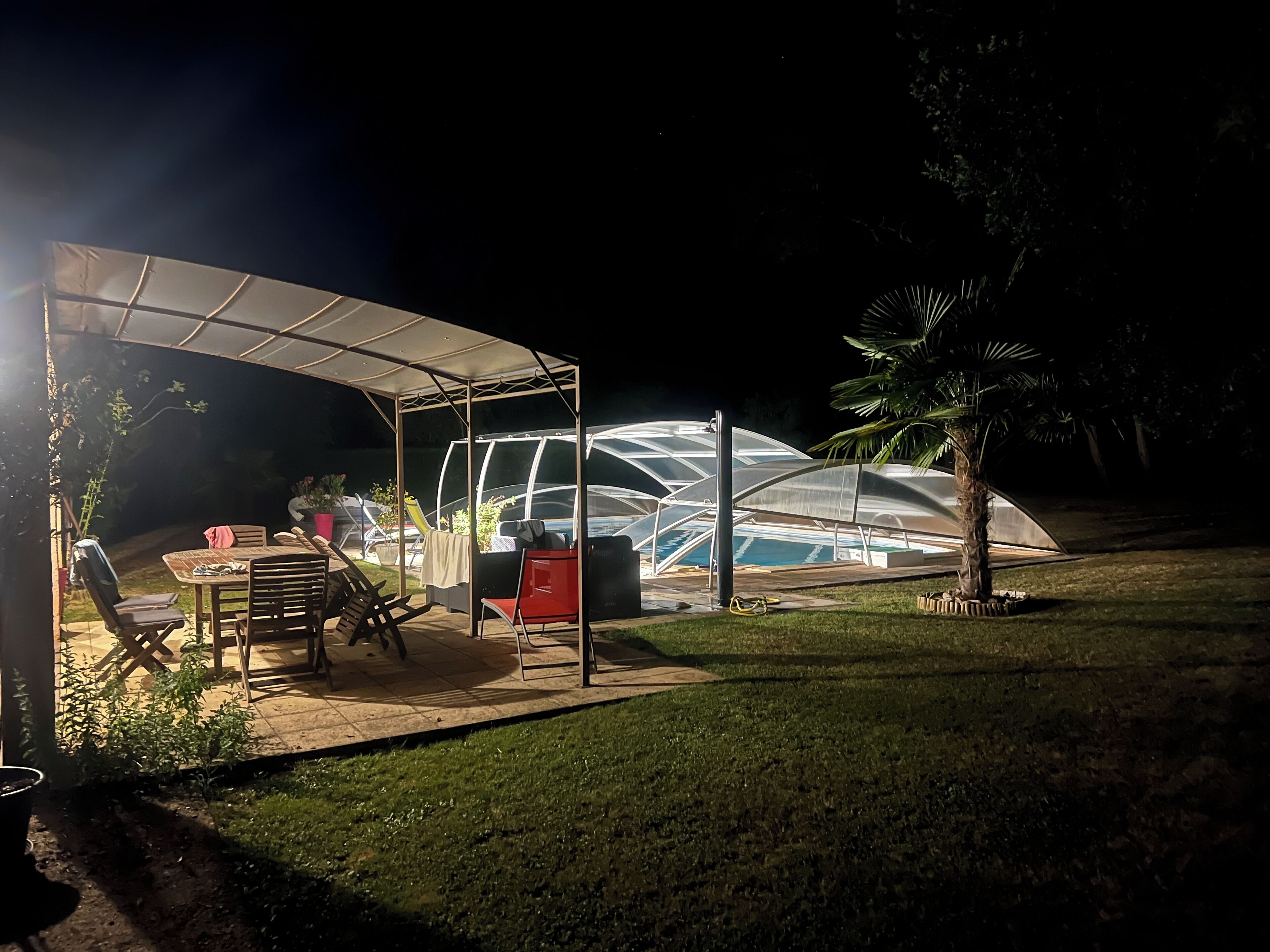 Un área de estar al aire libre techada, con piscina y una estructura tipo invernadero.