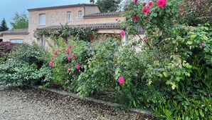 Un bâtiment avec un toit en tuiles et un jardin où poussent des fleurs roses.