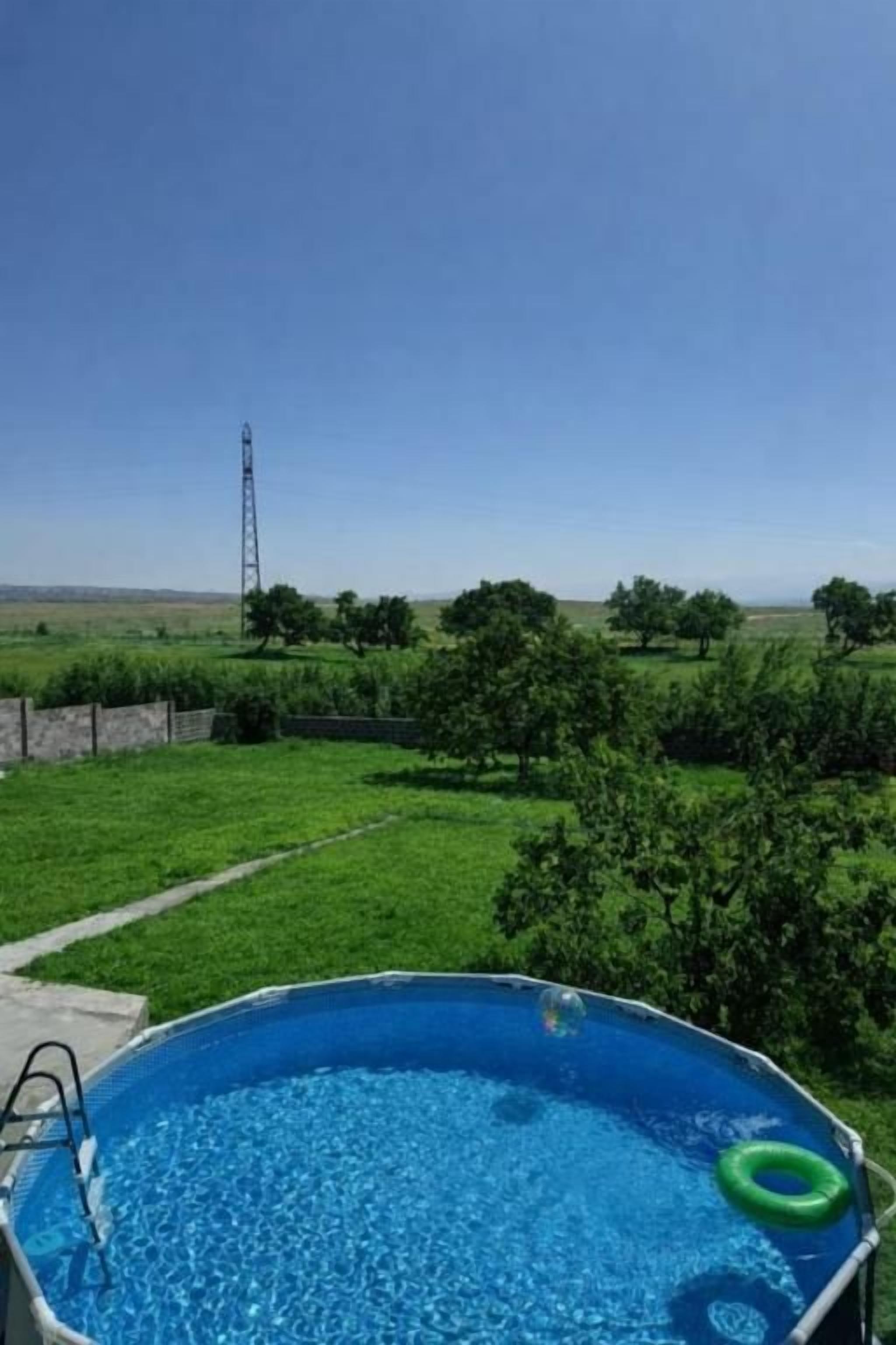 Une piscine avec un escalier, entourée d’une pelouse, d’arbres et sous un ciel dégagé.