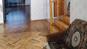 A living room with a herringbone floor, a wooden staircase, and a patterned throw on a brown sofa. - Airport to Echmiadzin Guest House (Parakar)