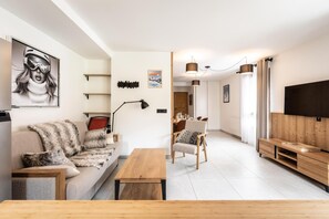 A modern living room with a sofa, a coffee table, a TV, and a dining area with chairs and a table.