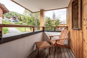 A wooden balcony with a chair and a small table, overlooking a residential area with houses and trees. - 50m from ski slopes, 1st floor, balcony, tv, 57m², Montalbert (La Plagne)