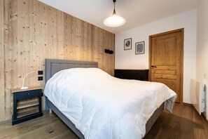 A bedroom with a bed, a nightstand, a wall-mounted light, and a wooden door.