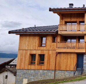Una casa a due piani in legno con fondamenta in pietra, un balcone al piano superiore e un piccolo ingresso.